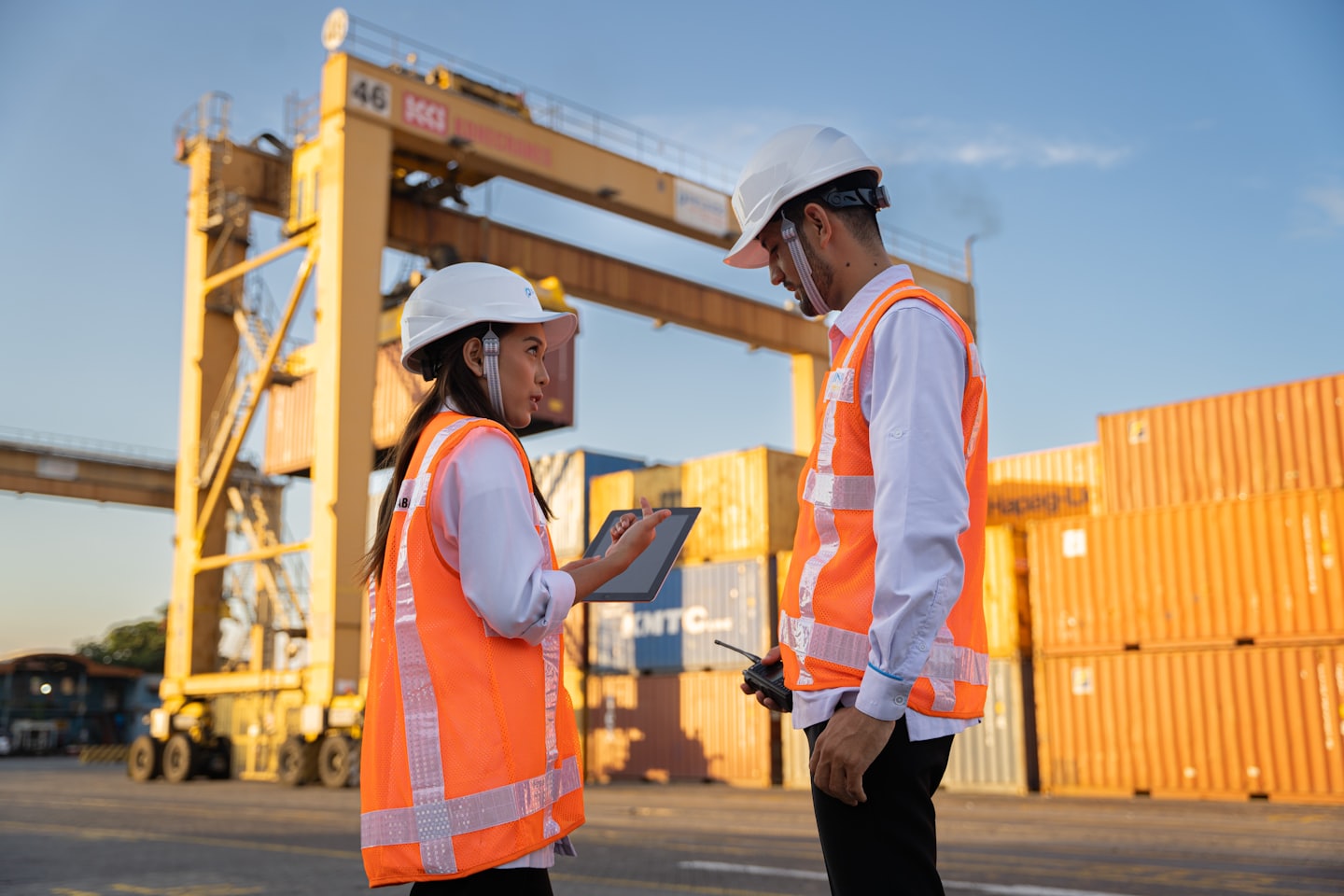 Twee logistieke medewerkers bespreken havenoperaties met containers en kranen.