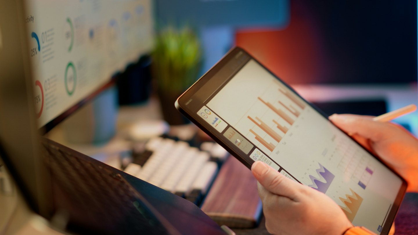 Persoon die bedrijfsanalyses op een tablet op een bureau bekijkt.
